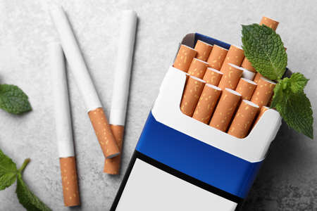 Pack of menthol cigarettes and mint leaves on gray table, flat layの写真素材