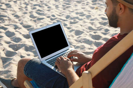 Man working with laptop in deck chair on beach, closeupの写真素材