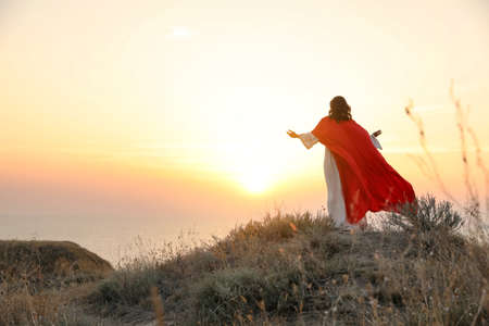 Jesus Christ raising hands on hills at sunset, back view. Space for textの写真素材