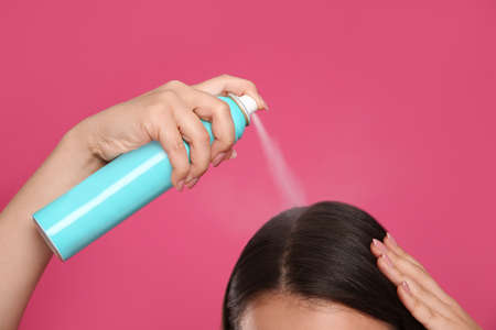 Young woman applying dry shampoo against pink background, closeupの写真素材