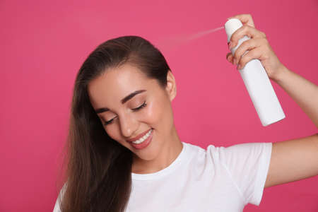 Young woman applying dry shampoo against pink backgroundの写真素材
