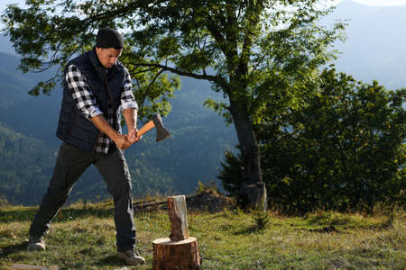 Handsome man with ax cutting firewood in mountainsの写真素材