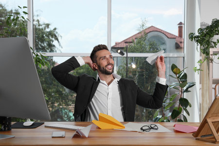 Handsome businessman playing with paper plane at desk in officeの写真素材