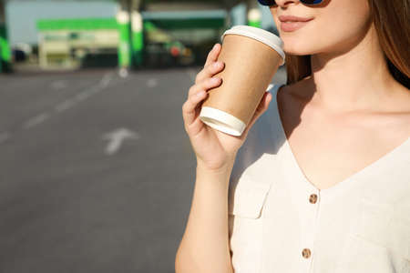 Beautiful young woman drinking coffee at gas station, closeup. Space for textの写真素材