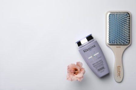MYKOLAIV, UKRAINE - SEPTEMBER 07, 2021: Kerastase shampoo, hair brush and beautiful flower on light background, flat lay. Space for textのeditorial素材