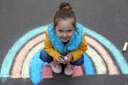Happy child near chalk drawing of rainbow on asphalt, above viewの写真素材