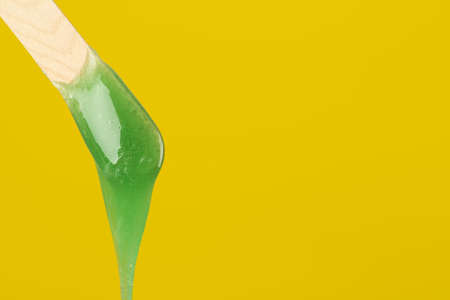 Wooden spatula with hot depilatory wax on yellow background. Space for textの写真素材
