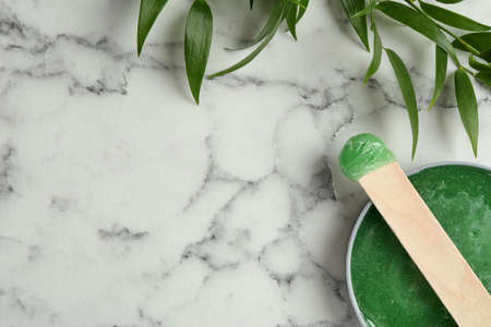 Spatula with wax and leaves on white marble table, flat lay. Space for textの写真素材