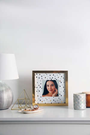 Photo frame with portrait of beautiful young woman near stylish decor on white tableの写真素材