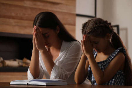 Young woman with her little daughter praying together over Bible at homeの写真素材