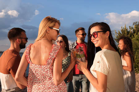 Group of friends with drinks having fun near river at summer party