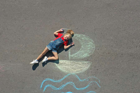 Cute little child lying near chalk drawing of boat on asphalt, top viewの写真素材