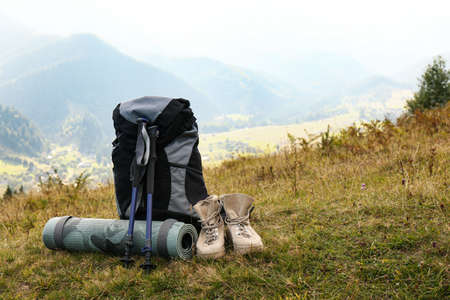 Backpack, trekking poles, boots and sleeping mat on hill, space for text. Tourism equipmentの写真素材
