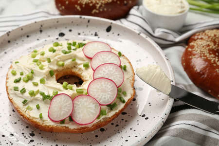 Delicious bagel with cream cheese, green onion and radish on plate, closeupの写真素材
