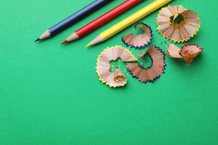 Color pencils and shavings on green background, flat lay. Space for textの写真素材