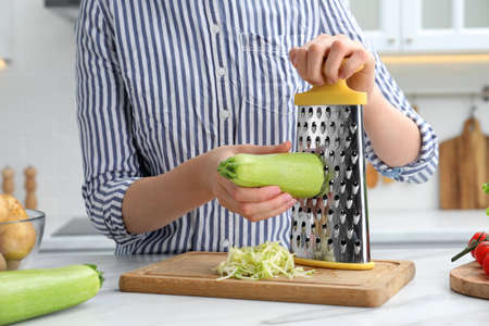 Woman grating zucchini at kitchen table, closeupの写真素材