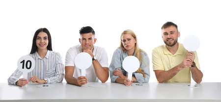 Panel of judges with different emotions holding blank signs at table on white background. Space for textの写真素材