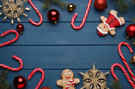 Frame of tasty candy canes and Christmas decor on blue wooden table, flat lay. Space for textの写真素材