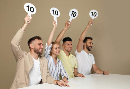 Panel of judges holding signs with highest score at table on beige backgroundの写真素材