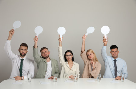 Panel of disappointed judges holding blank score signs at table on beige background. Space for textの写真素材