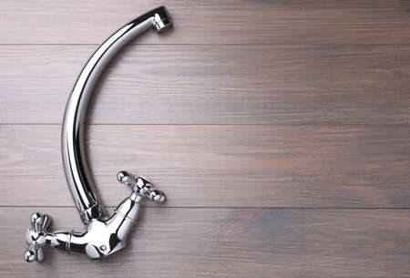 Double handle water tap on wooden table, top view. Space for text