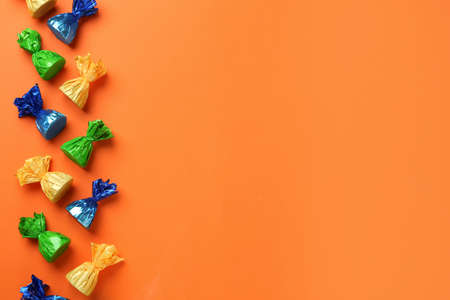 Many candies in colorful wrappers on orange background, flat lay. Space for textの写真素材