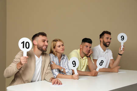 Panel of judges holding different score signs at table on beige backgroundの写真素材