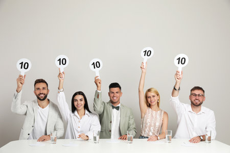 Panel of judges holding signs with highest score at table on beige backgroundの写真素材