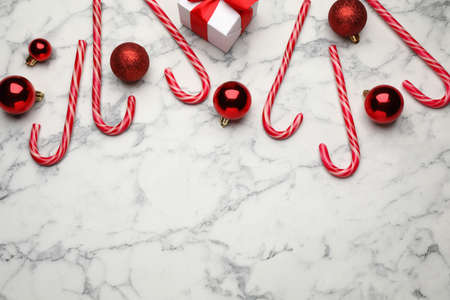 Tasty candy canes, Christmas balls and gift box on white marble table, flat lay. Space for textの写真素材