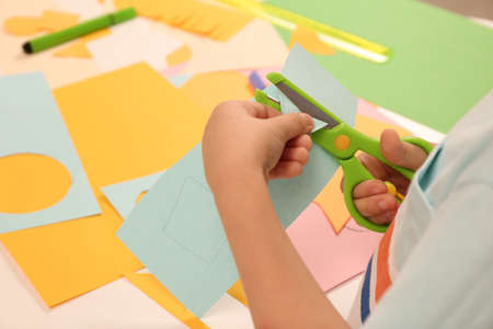 Little boy cutting color paper with scissors at table indoors, closeupの写真素材