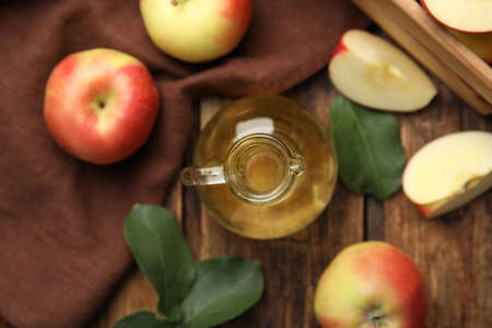 Natural apple vinegar and fresh fruits on wooden table, flat lay