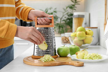 Woman grating fresh green apple at kitchen counter, closeupの写真素材