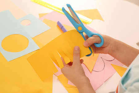 Little boy cutting color paper with scissors at table indoors, closeupの写真素材