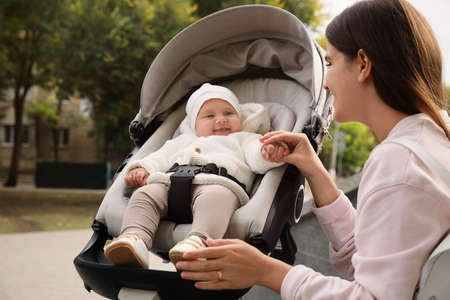Young mother with her adorable baby in stroller outdoors