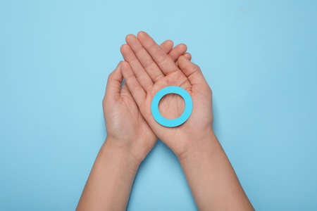 Woman showing blue paper circle as World Diabetes Day symbol on color background, top view