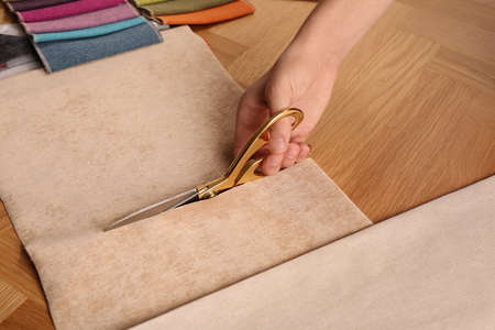 Man cutting beige fabric with scissors at wooden table, closeup