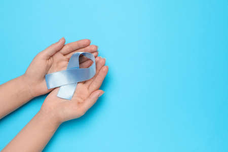 Woman holding light blue awareness ribbon on color background, top view. Space for textの写真素材