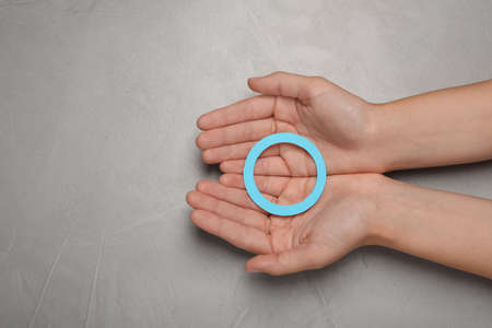 Woman holding blue paper circle as World Diabetes Day symbol at gray table, top view with space for...