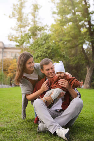 Happy parents with their adorable baby on green grass in parkの写真素材