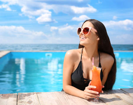 Beautiful young woman with cocktail in outdoor swimming pool at luxury resort