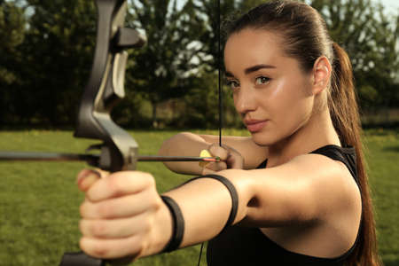 Woman with bow and arrow practicing archery in parkの写真素材