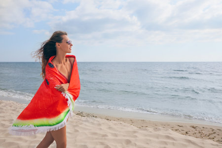 Beautiful woman with bright beach towel on seashoreの写真素材