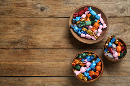 Candies in colorful wrappers on wooden table, flat lay. Space for textの写真素材