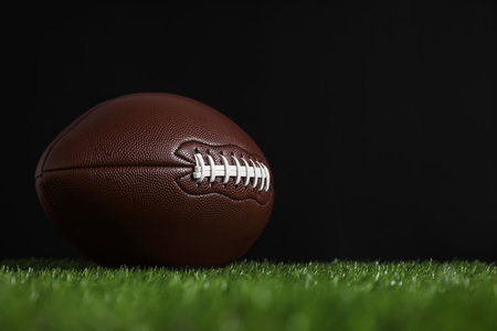 American football ball on green grass against black background. Space for textの写真素材