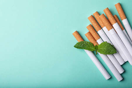 Menthol cigarettes and mint on turquoise background, flat lay. Space for textの写真素材
