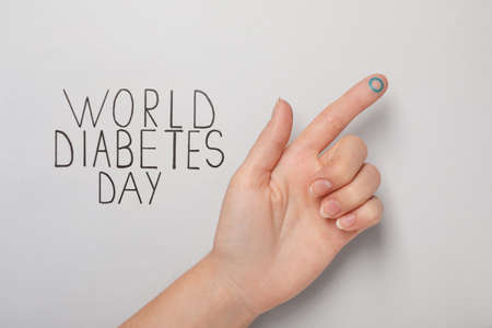 Woman showing finger with drawn blue circle near text World Diabetes Day on light background, closeupの写真素材