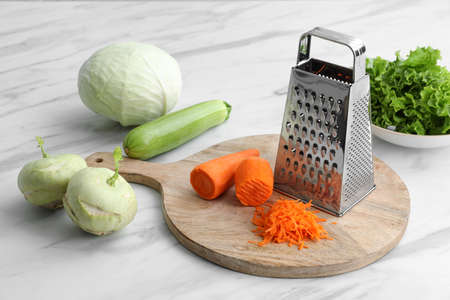 Grater and fresh vegetables on white marble tableの写真素材
