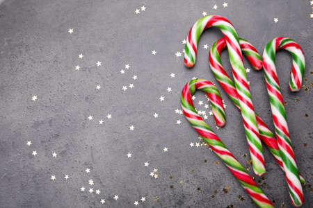 Many sweet Christmas candy canes and shiny confetti on gray background, flat lay. Space for textの写真素材