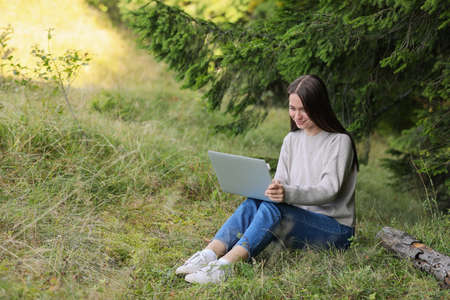 Young woman working on laptop in forest, space for textの写真素材