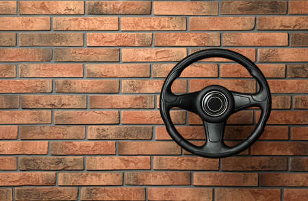 New black steering wheel near red brick wall, space for textの写真素材